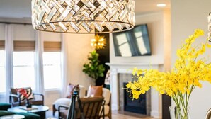 A modern living room with a fireplace, a hanging light fixture, and a vase of yellow flowers. - Brand New-Downtown Apex-4BD/4BA-Gameroom-2 Kings! (Apex)