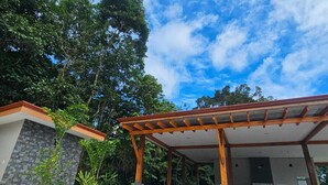 A swimming pool with a covered patio area, surrounded by lush greenery and a clear blue sky.