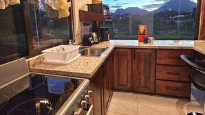 A kitchen with a stove, sink, and a large window overlooking a mountainous landscape.