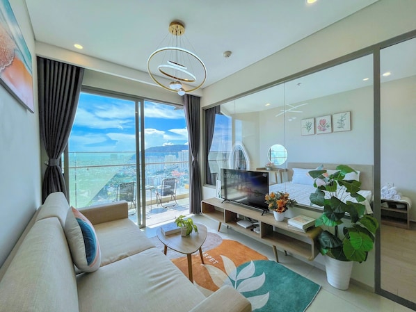 A modern living room with a sofa, a coffee table, a TV, and a large window offering a city view. - The Song Vung Tau An An Homestay (Ho Chi Minh City)