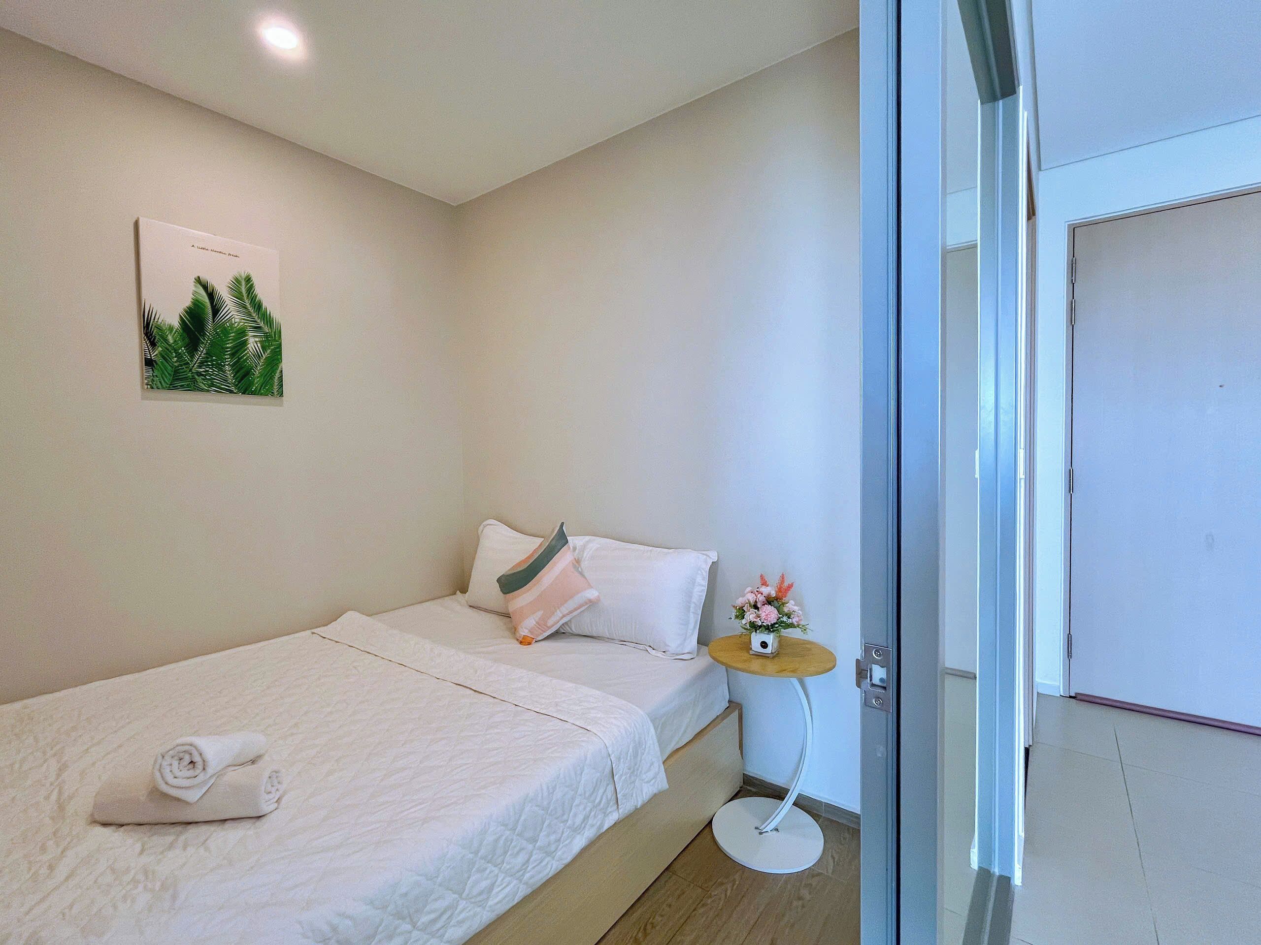 A single bed with a neatly folded towel, a small round table with a flower arrangement, and a framed picture on the wall.