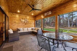 A wooden cabin interior with a sofa, dining table, chairs, and large windows offering a view of the outdoors. - Lakeview Home with Dock on the Whitefish Chain, Outdoor Pool, Pickleball & More (Pequot Lakes)