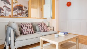 A modern living room with a grey sofa, patterned cushions, a wooden coffee table, a mirror, and a framed artwork on the wall. - Blueground | Ternes, elevator & w/d, nr Arc (Paris)