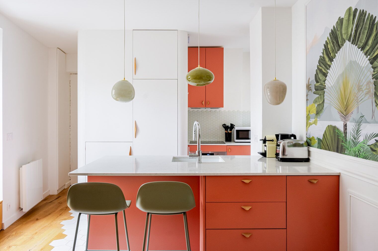 A modern kitchen with a white countertop, red cabinets, and two green bar stools.