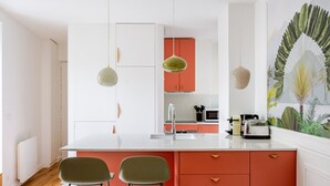 A modern kitchen with a white countertop, red cabinets, and two green bar stools. - Blueground | Ternes, elevator & w/d, nr Arc (Paris)