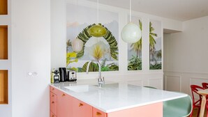 A kitchen with a white countertop, pink cabinets, and a window with a tropical mural. - Blueground | Ternes, elevator & w/d, nr Arc (Paris)