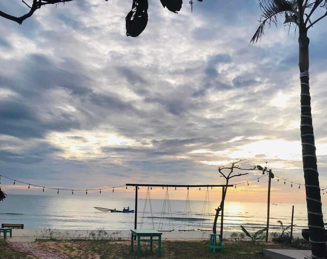 Escena de playa con una hamaca, sillas y una palmera.