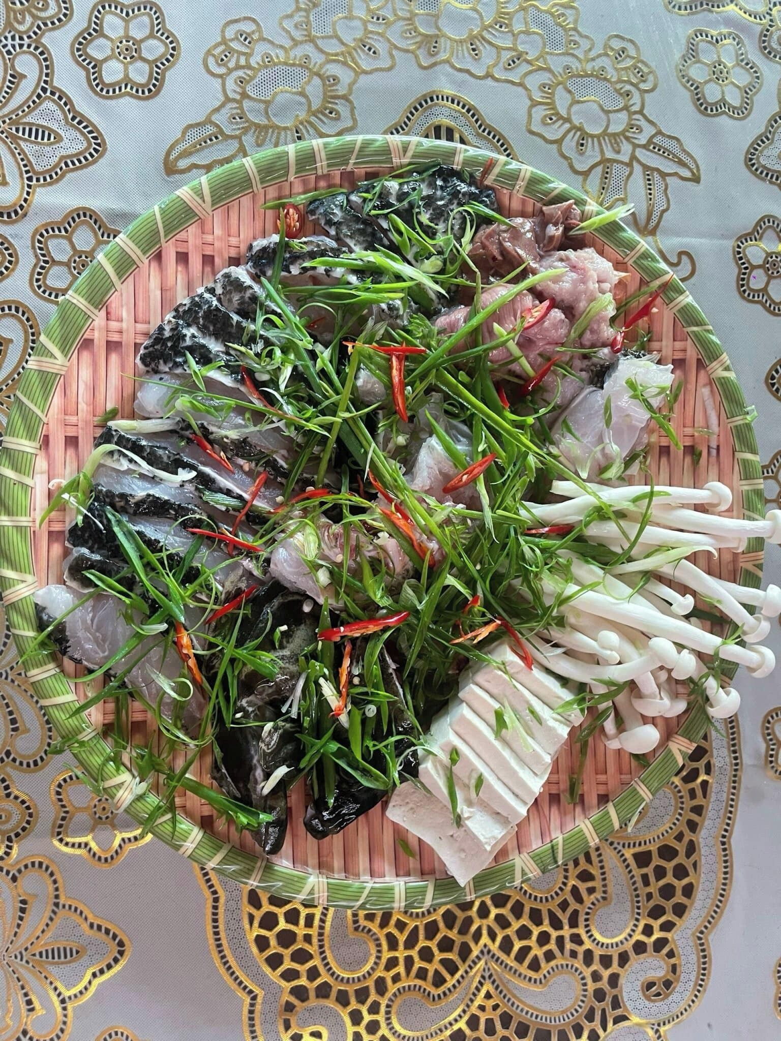 Una cesta tejida llena de mariscos y verduras, colocada sobre una mesa con mantel estampado.