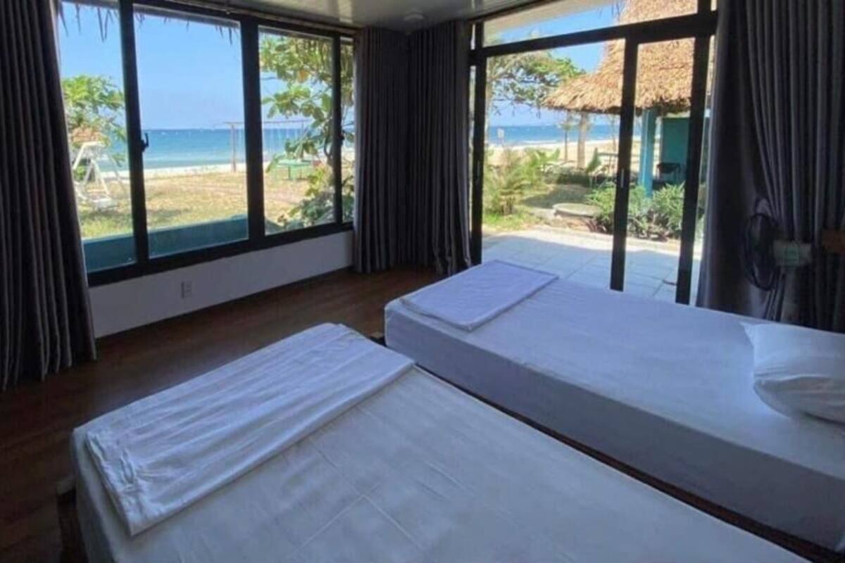 A room with two beds, large windows, and a view of the beach.