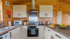 Una cocina moderna con paredes de madera, armarios blancos, electrodomésticos de acero inoxidable y una isla central con frutas y una cesta de pan.