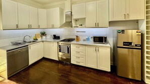 A modern kitchen with white cabinets, stainless steel appliances, and a wooden floor. - Comfy family home(15 mins to CBD & beach) (South Plympton)