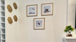 A corner of a room with a grey upholstered chair, a checkered pillow, and three framed pictures on the wall. - Comfy family home(15 mins to CBD & beach) (South Plympton)