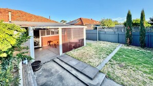 A backyard with a covered patio, a wooden table, and a barbecue area. - Comfy family home(15 mins to CBD & beach) (South Plympton)