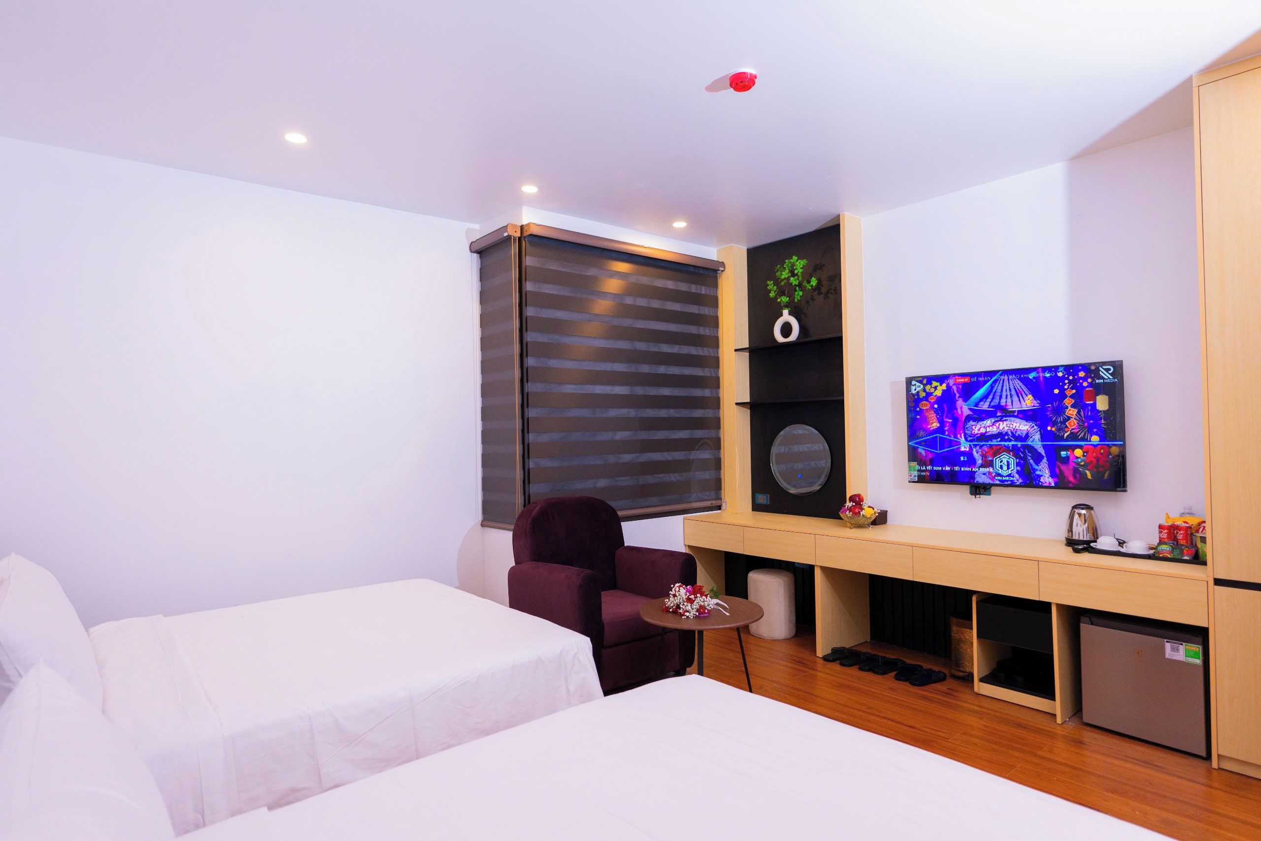 Une chambre d’hôtel avec deux lits, un bureau avec une télévision, une chaise et une petite table agrémentée d’un arrangement floral.