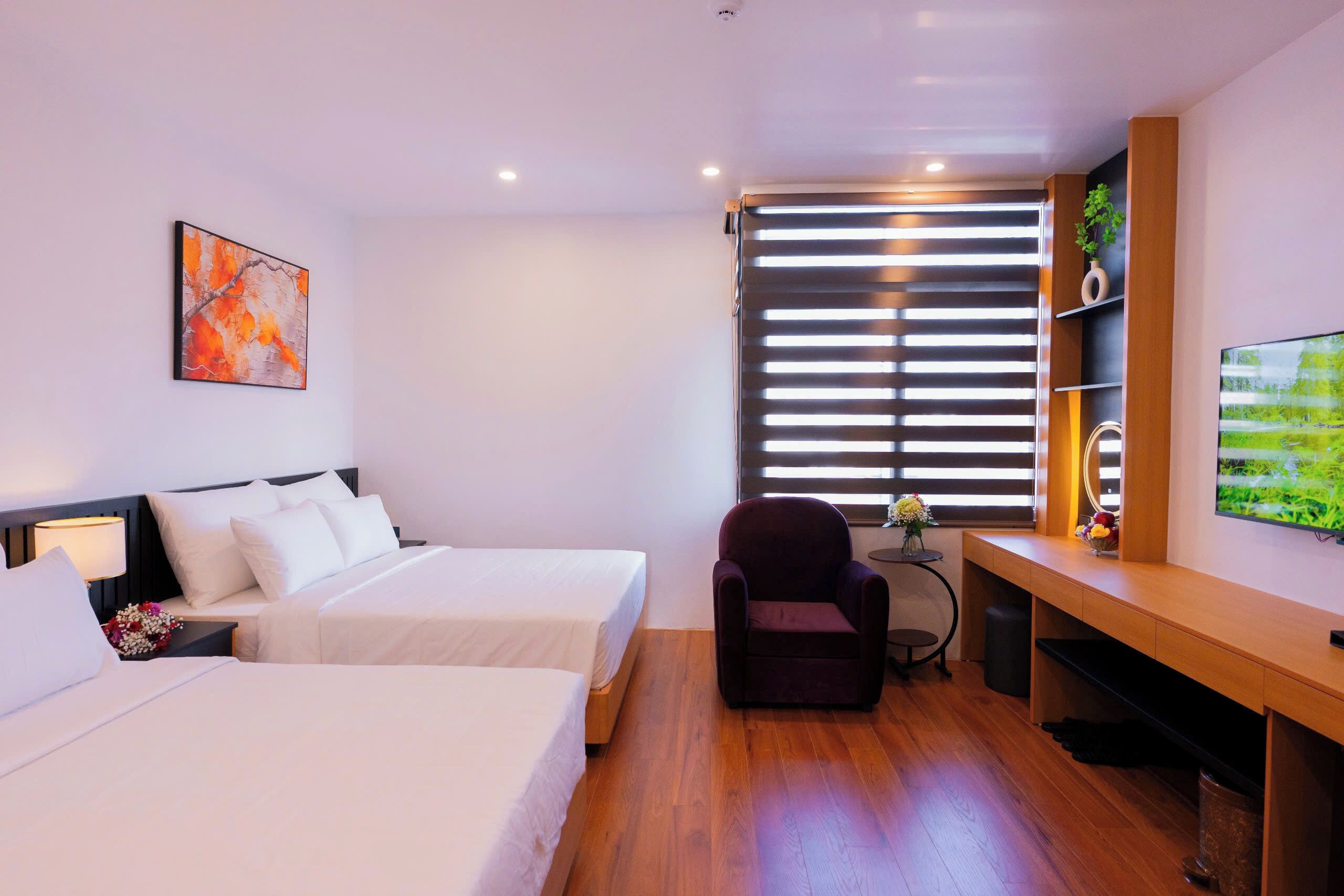 Habitación de hotel con dos camas, un escritorio, una silla, un televisor, una ventana con persianas y un cuadro en la pared.
