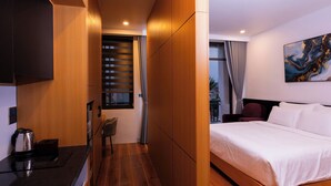 A modern hotel room with a large bed, a desk with a kettle, a chair, and a window with curtains. - CELINA HOTLE Ninh Bình (Hoa Lu)