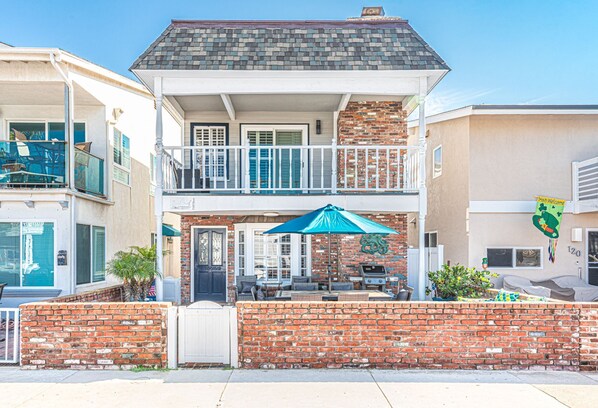 A two-story building with a balcony, a brick facade, and a blue umbrella.
