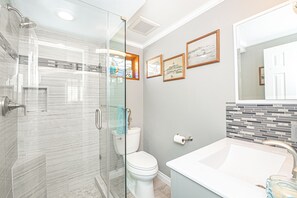 A modern bathroom with a glass shower enclosure, a toilet, a sink with a large basin, and a tiled backsplash.