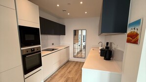 A modern kitchen with white cabinetry, a black microwave, and a coffee machine. - Apt Sleeps 6 With Two Bathrooms (Manchester)