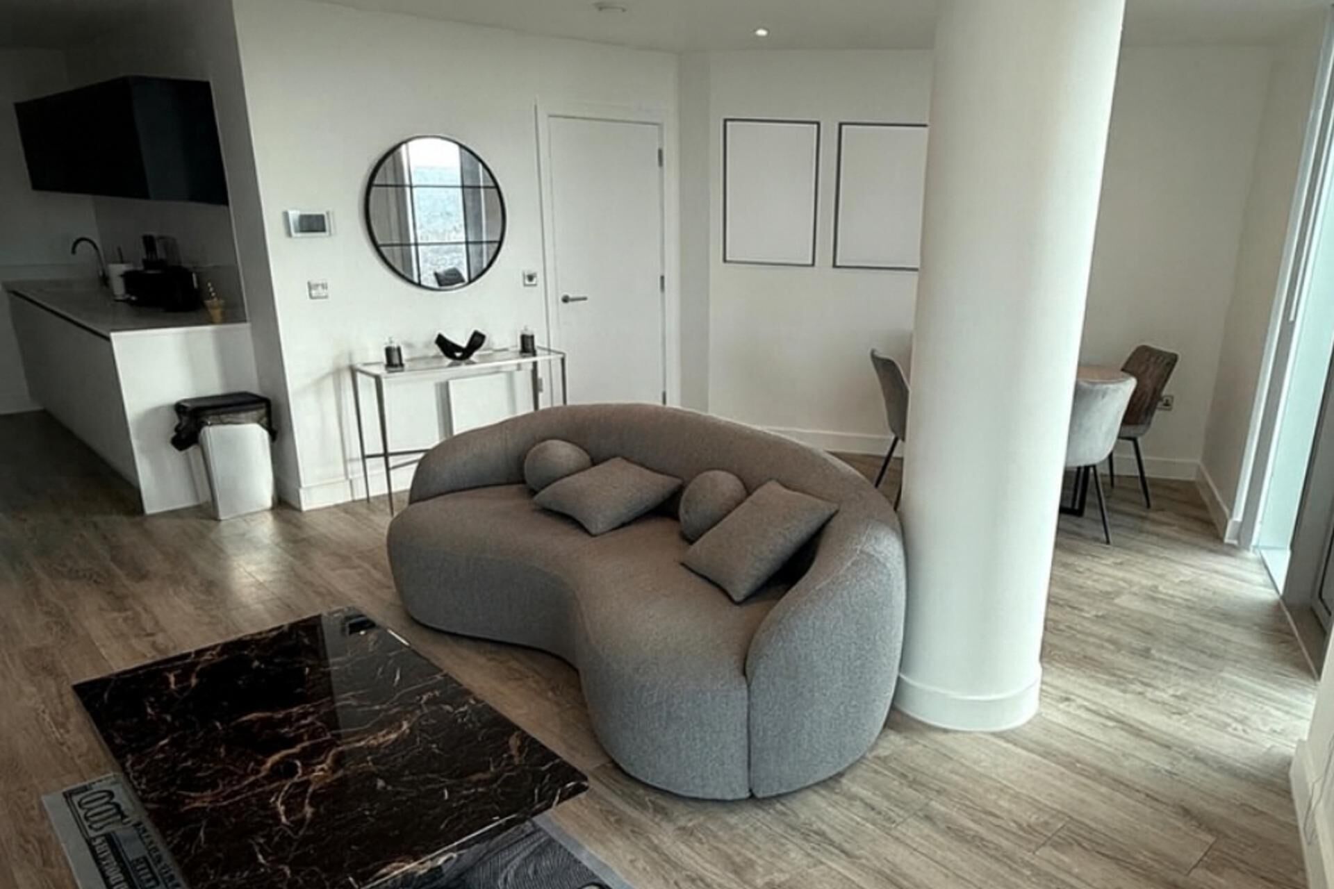 A modern living room with a curved sofa, a round mirror, and a minimalist design.