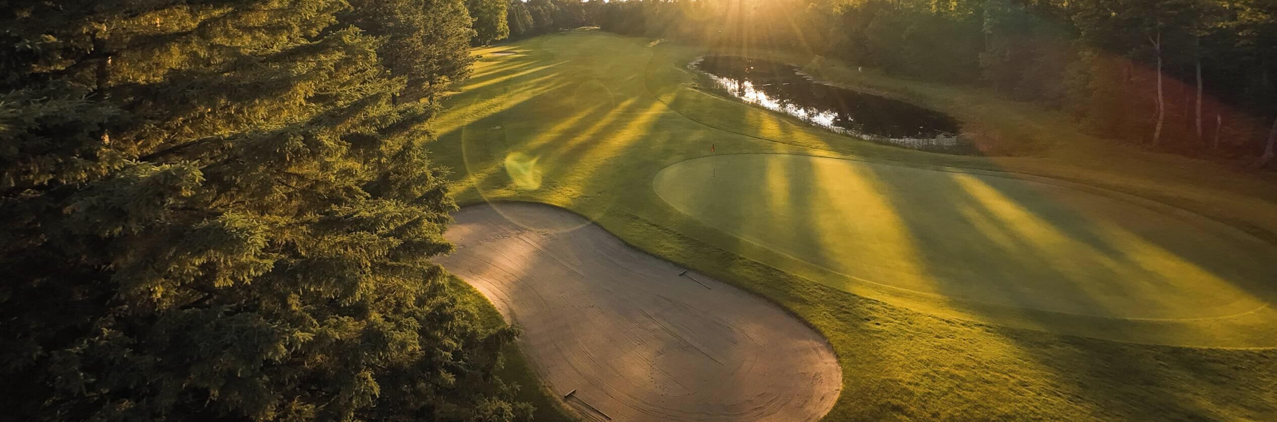 En golfbana med ett vattenhinder, en sandbunker och en flaggstång.