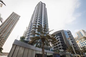 A high-rise building with multiple balconies, surrounded by other buildings and palm trees.