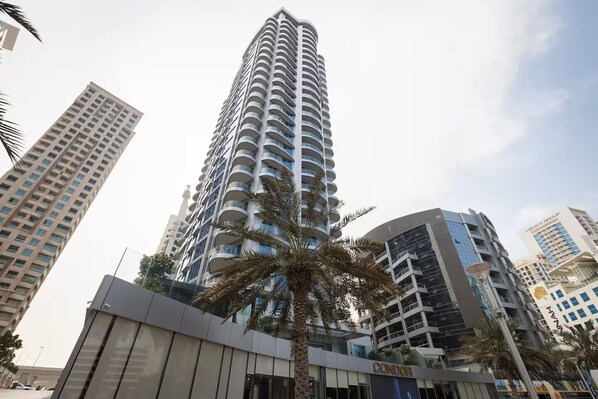 A high-rise building with multiple balconies, surrounded by other buildings and palm trees.