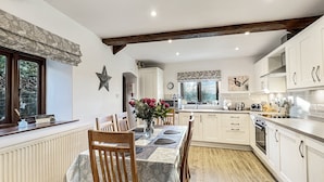 A modern kitchen with white cabinets, a wooden dining table with chairs, and a window with a view of trees. - The Cider Barn, Waterrow, Nr Wivelsicombe (Waterrow)