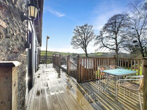 Een houten terras met een jacuzzi, rieten stoelen en een stenen muur.