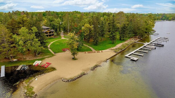 A lakeside property with a dock, a grassy area with chairs, and a building surrounded by trees.