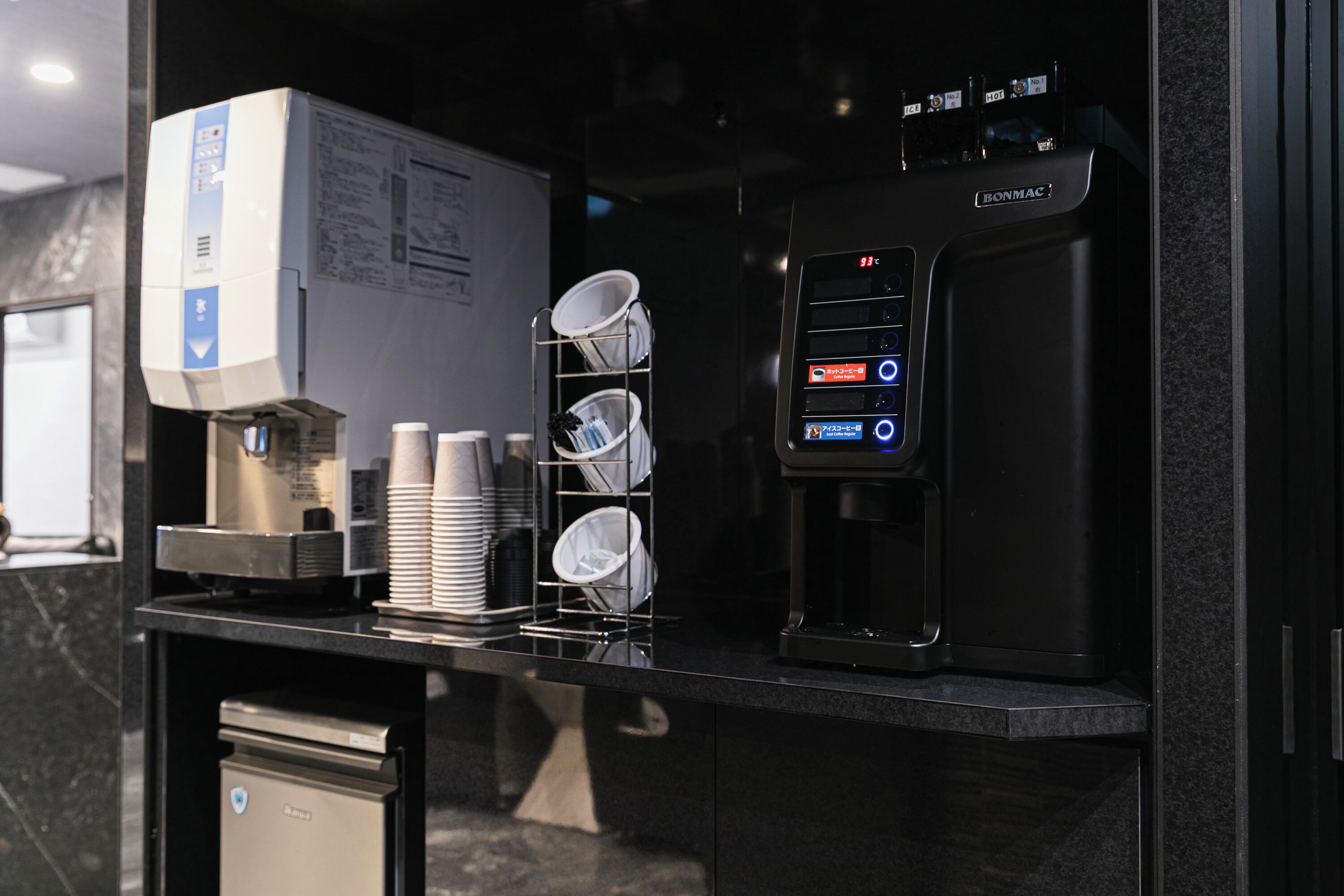 Une machine à café, une pile de gobelets jetables et un égouttoir sur un comptoir.