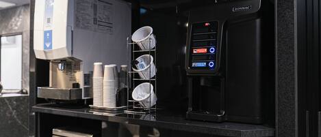 A coffee machine, a stack of disposable cups, and a dish rack on a counter.