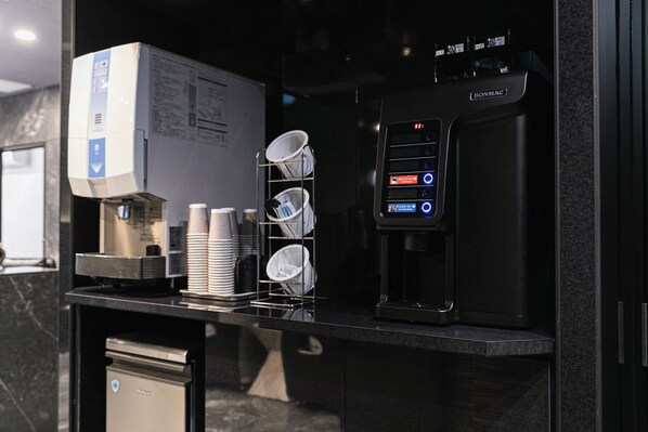 A coffee machine, a stack of disposable cups, and a dish rack on a counter.