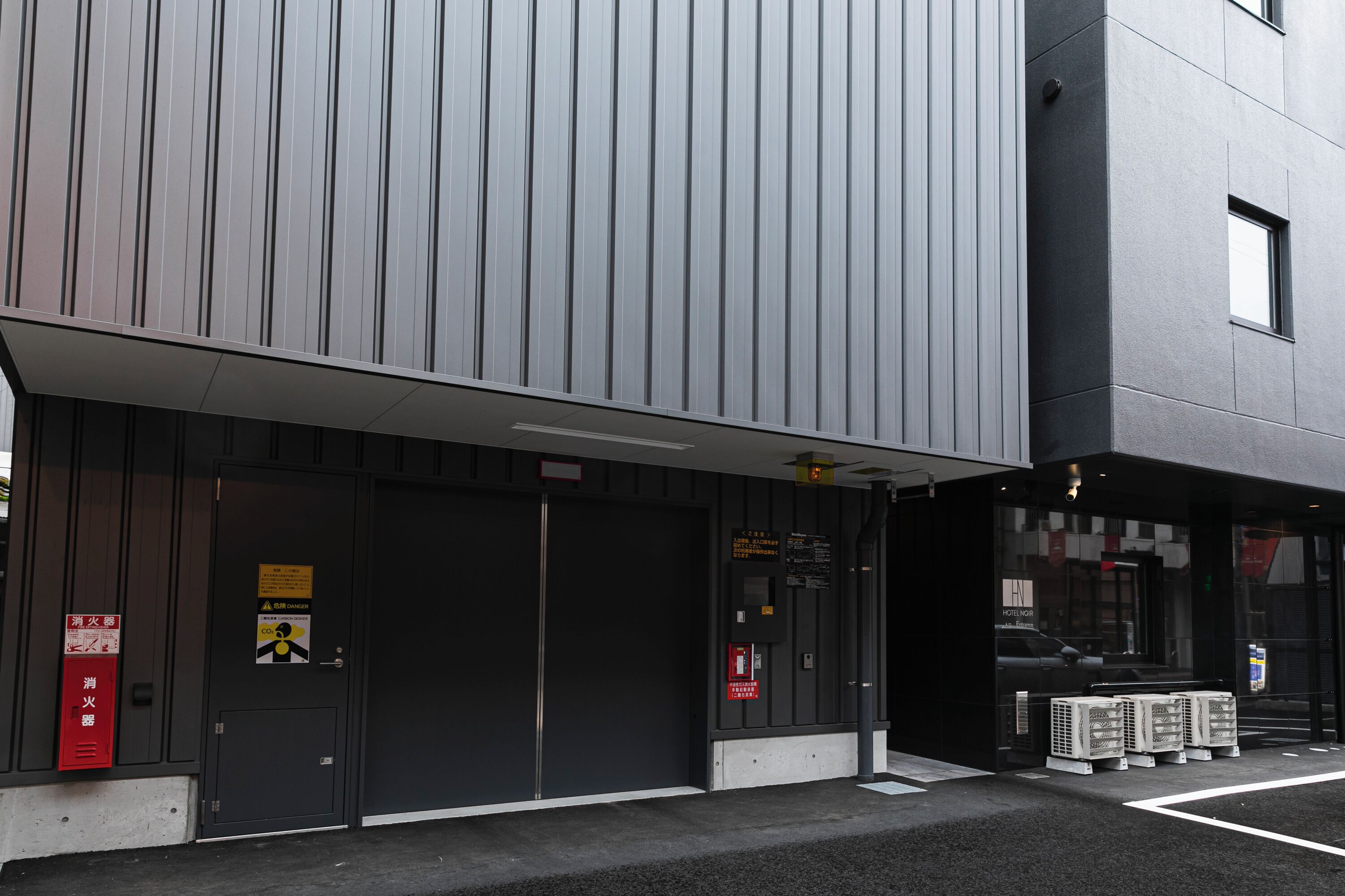 A modern building with two large doors, a fire extinguisher, and a sign indicating a fire exit.