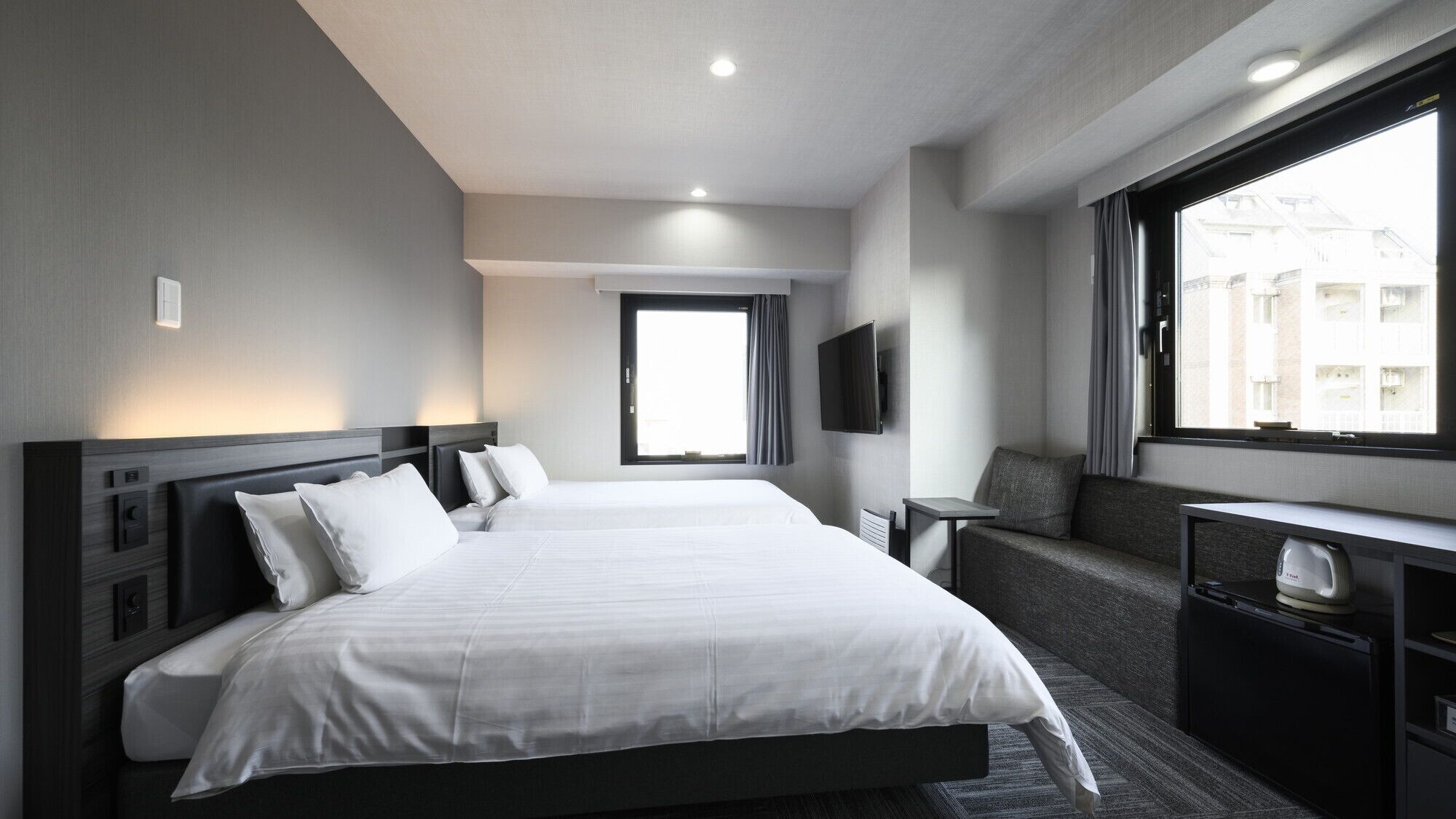 Une chambre d’hôtel avec un grand lit, une télévision, un coin salon et une fenêtre donnant sur des immeubles.