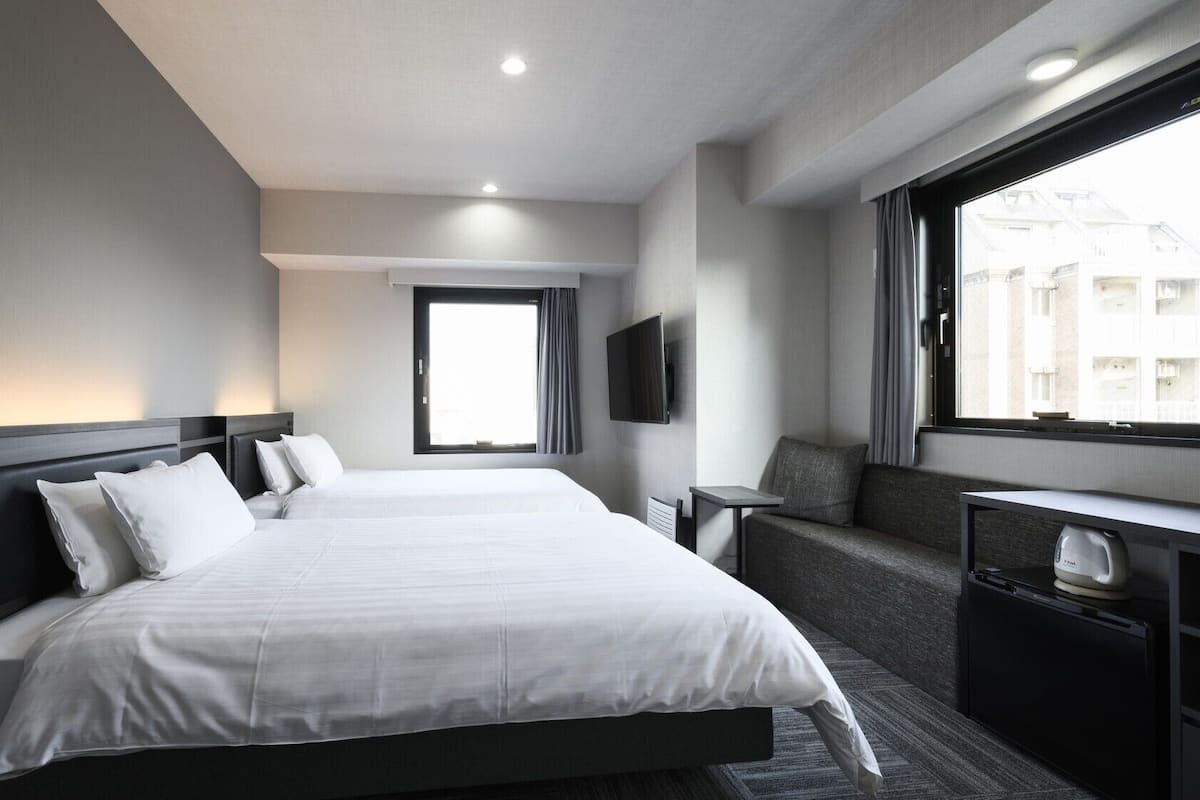 Une chambre d’hôtel avec un grand lit, une télévision, un coin salon et une fenêtre donnant sur des immeubles.