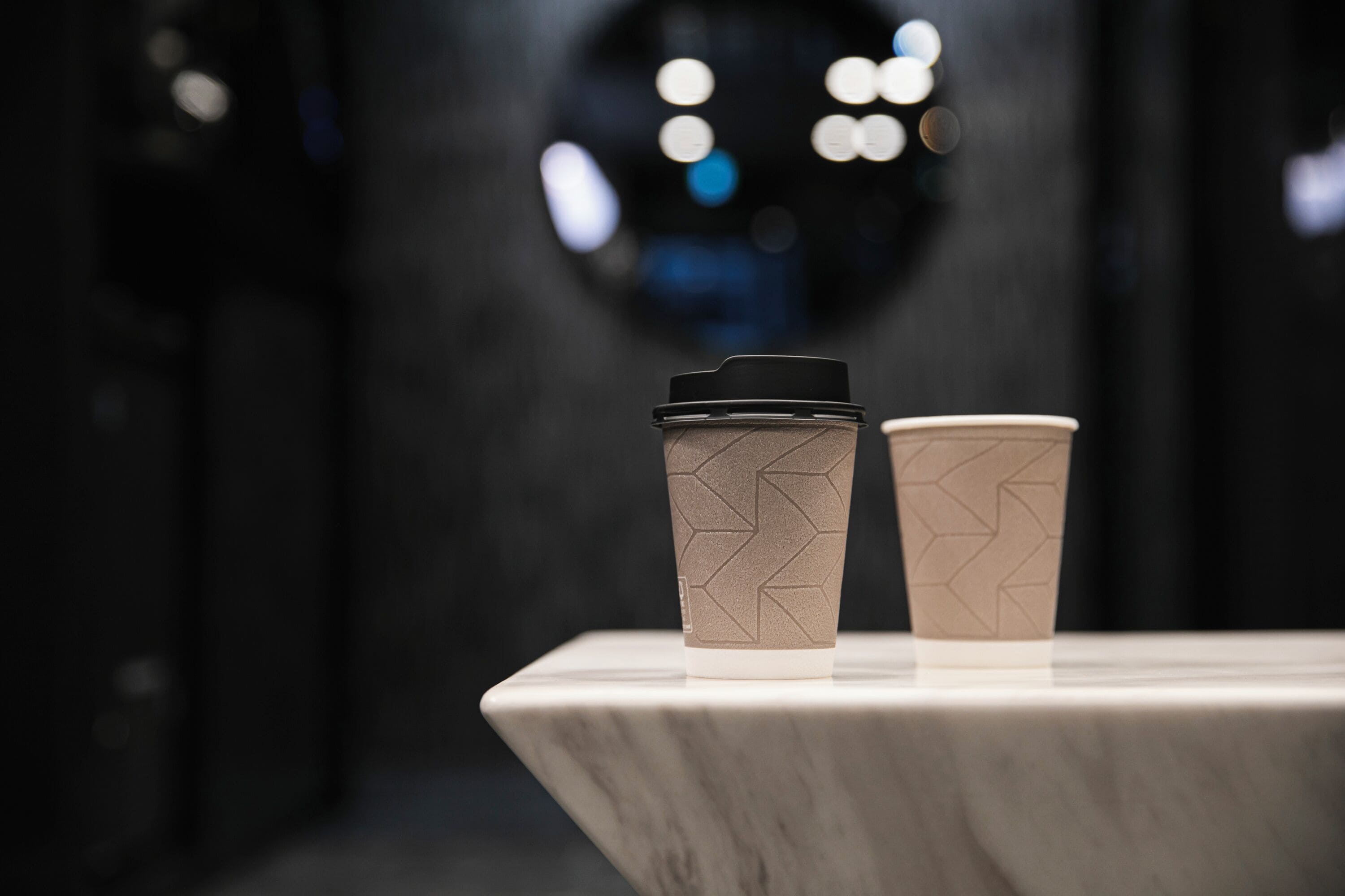 Dos vasos de café desechables con tapas sobre una superficie de mármol.