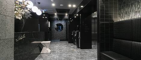 A modern lobby with a marble floor, a reception desk, a seating area, and a wall-mounted digital display.
