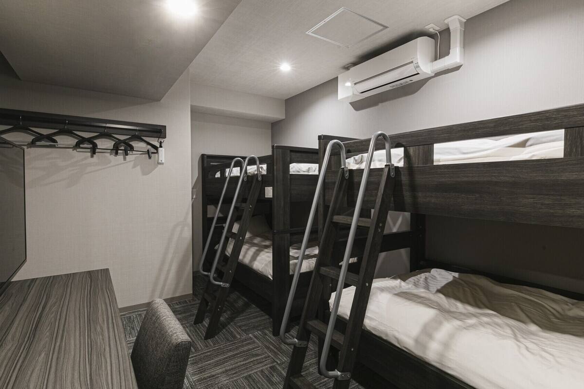 A room with bunk beds, a desk, and a hanging coat rack.