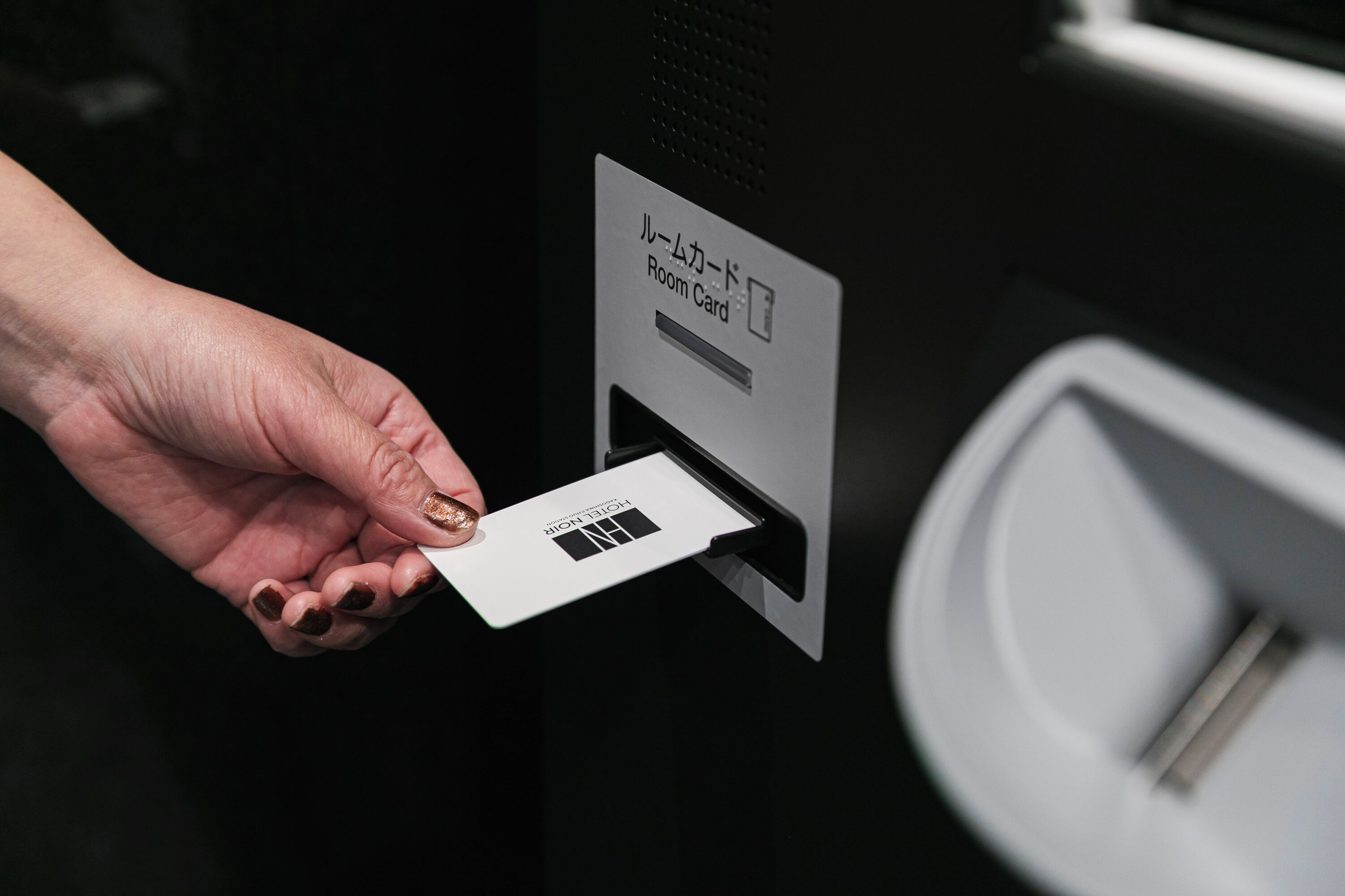 A hand inserting a room card into a slot labeled "Room Card" with Japanese text.
