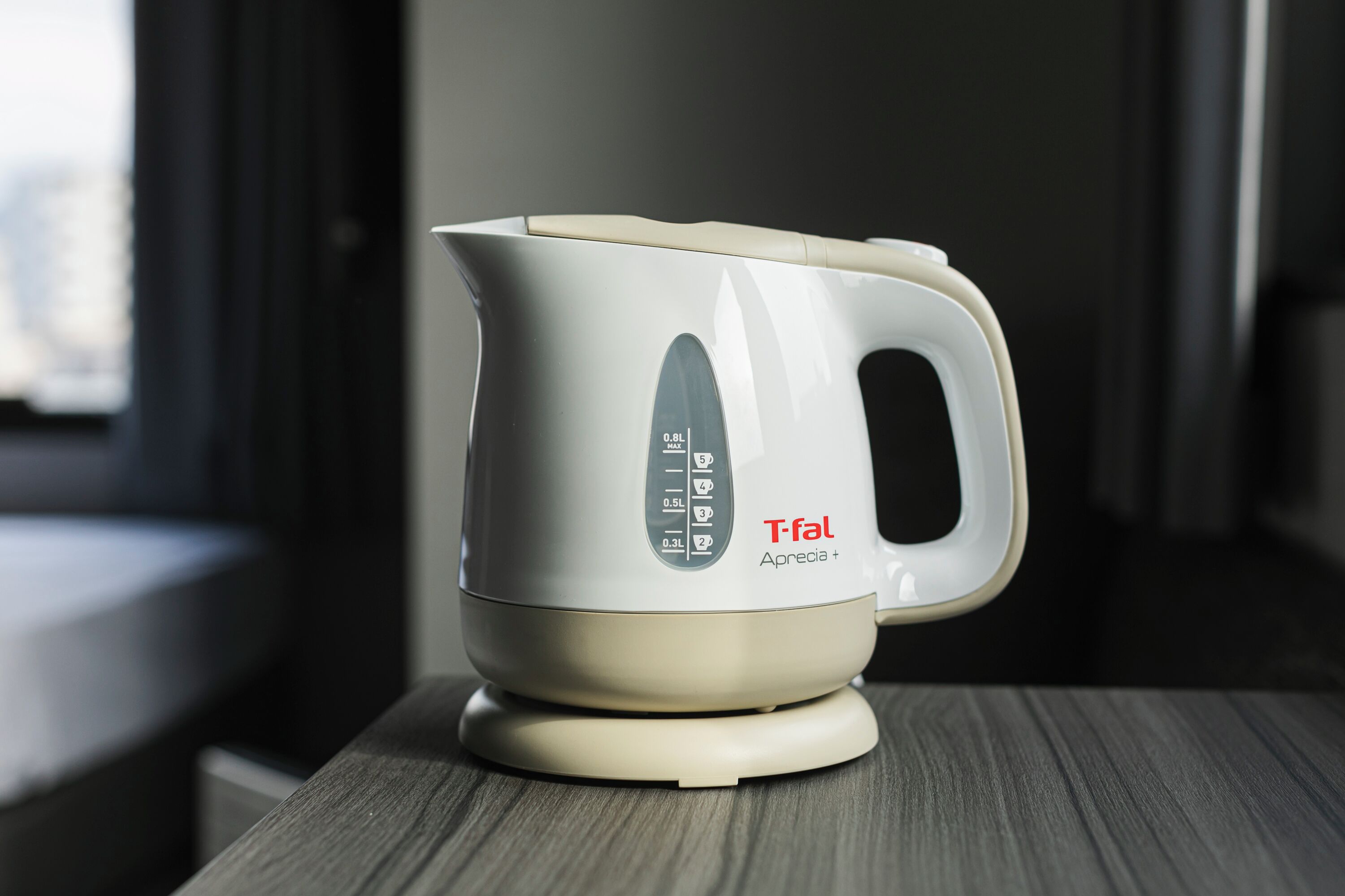 A white electric kettle with a handle and control panel on a wooden surface.