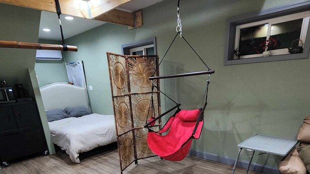 Een kamer met een bed, een hangstoel, een kleine tafel en een televisie aan de muur.