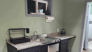 Une cuisine compacte dotée d’une cuisinière, d’un évier et d’un lave-vaisselle intégrés, avec des meubles de rangement aux couleurs sombres et un plan de travail en granit.
