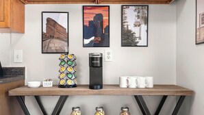Una encimera de cocina con una cafetera, tazas, un recipiente para azúcar y frascos con ingredientes.