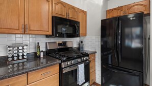 Una cocina con armarios de madera, una estufa de acero inoxidable, un microondas negro y un refrigerador negro.