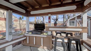 Un patio exterior con una parrilla, bancos de madera y piso de concreto.