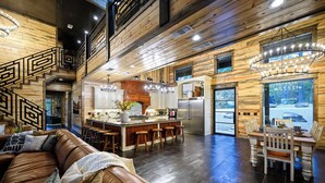 A spacious living area with a brown leather couch, wooden flooring, a kitchen with a central island, and a dining table with chairs. - Inspiration Point | 6 King Suites, 2 Bunk Rooms, Pool, 2 Hot Tubs, Pickleball & Creek Views (Broken Bow)