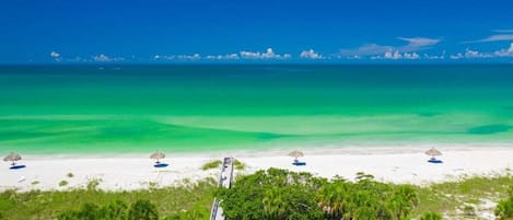Ein Strand mit klarem türkisblauem Wasser, weißem Sand und grüner Vegetation.