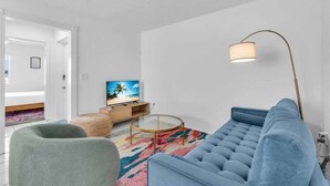A modern living room with a sofa, a round coffee table, a television, and a floor lamp. - Walk to Lido Beach Tiki Bar, 2 Queen Suites (Sarasota)