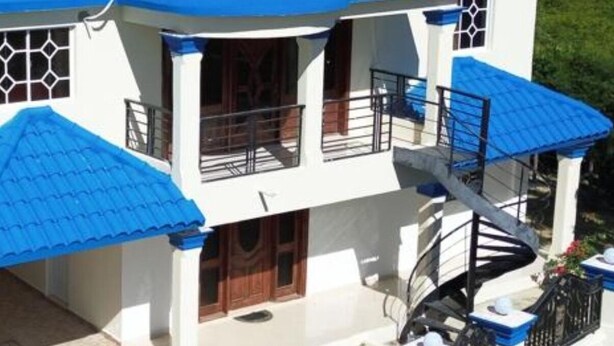 A two-story building with a red-tiled roof, blue awnings, and a spiral staircase. - Homes for rent vacation rentals vacation rentals los Conuco de Villavaquez (Monte Plata)